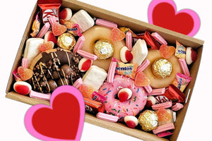 Valentine’s Sweet Treat Box featuring 4 Krispy Kreme donuts topped with KitKat Minis, white TimTams, sour heart lollies, mini musk sticks, strawberries & cream Allens lollies, Mentos, and Ferrero Rocher chocolates, presented in a 25x16x8 cm gift box.