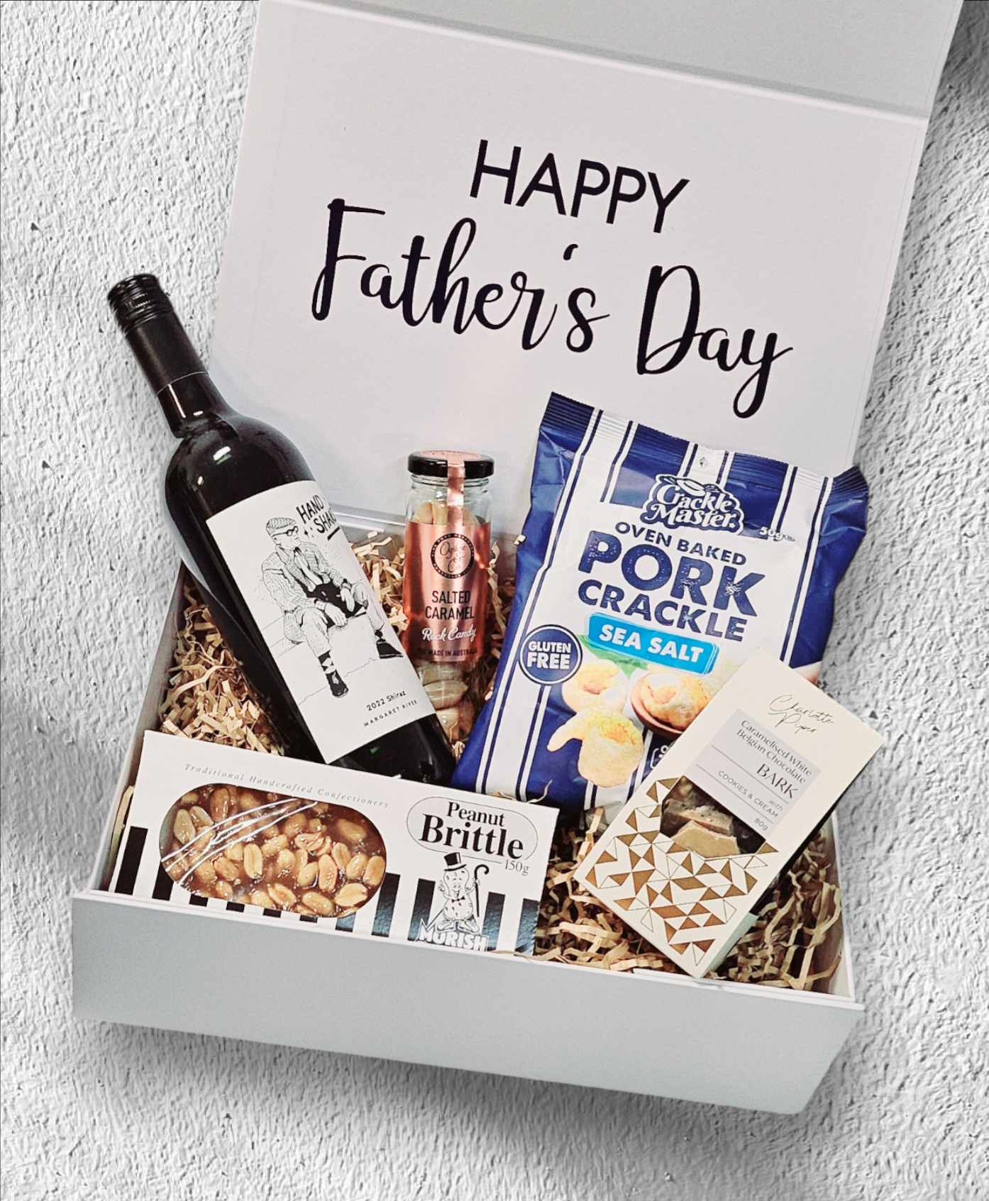 Father’s Day Box 1 featuring Handshake Red Wine from Margaret River, Salted Caramel Boiled Lollies, Sea Salt Pork Crackle, Morish Nute Peanut Brittle, and Caramel Chocolate Bark, all presented in a stylish gift box.