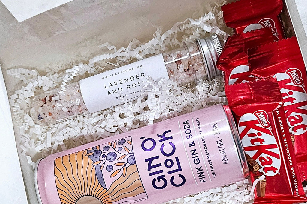 A charming Gin O'Clock gift package featuring a 250ml can of Gin O'clock Pink Gin & Soda, a tube of botanical bath salts, and four 17g Kit Kat bars, beautifully arranged for a delightful treat perfect for mothers, sisters, best friends, or teachers.
