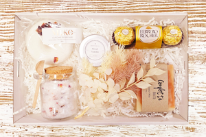 A soothing Soak and Relax box featuring lavender and rose bath salts for a serene soak, a playful donut bath bomb for a burst of fun, decadent Ferrero Rocher chocolates for indulgence, creamy coconut milk soap for skin pampering, vanilla lip balm for soft lips, and dried flowers for a touch of natural beauty, all beautifully arranged for a complete relaxation experience.
