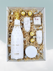 An elegant Soak and Sip Sparkling package featuring a 750ml bottle of Posh Plonk Shiraz, a 100g Candle Queens bath soak, a 200g scented candle, Ferrero Rocher chocolates, Hershey's Kisses, and two wine glasses, all beautifully arranged with signature confetti, a decorative bow, and a personalized message card for a perfect indulgent experience.
