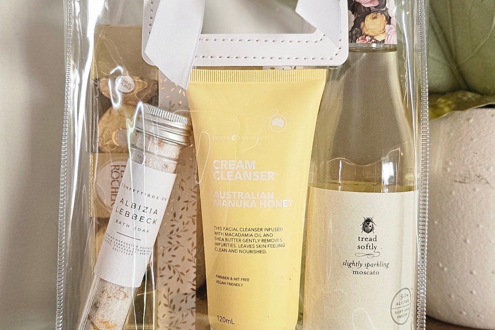 Sweet Serenity gift bag featuring a bottle of moscato wine, a box of Ferrero Rocher chocolates, a soothing bath soak, and a honey cleanser, all beautifully arranged in an elegant gift bag, perfect for relaxation and indulgence.