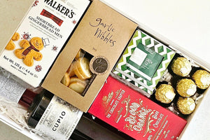 A Christmas hamper featuring Cupio Pinot Noir wine, Walkers shortbread biscuits, Ogilvie garlic nibbles, 5 Ferrero Rocher chocolates, Crunch Box blood orange chocolate, and a box of green tea, all beautifully packaged in a white magnet gift box.