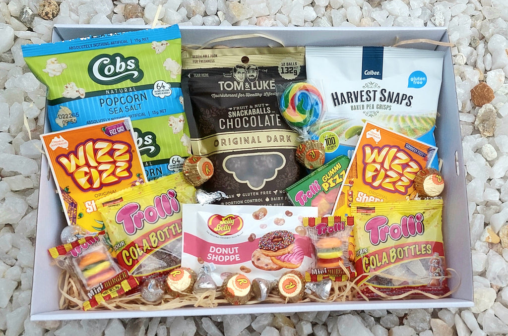 Gluten-Free Treats Box: Packed with a delicious variety of gluten-free snacks, both sweet and savory. Includes Cobs Sea Salt Popcorn, Tom & Luke Fruit & Nut Snackballs, Harvest Snaps Baked Pea Crisps, Jelly Belly Donut Shoppe, Wizz Fizz Sherbet, Trolli Sour Cola Bottles, Reese's Peanut Butter Cups, and Hershey's Kisses. Perfect for gluten-free indulgence!