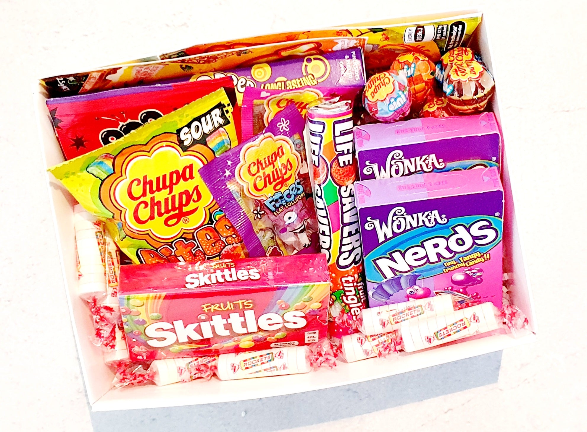 Mini Delight Gift Box: A sweet treat packed with 2 Nerds packs, 1 Skittles, 1 Sour Bites, 1 Pop Rock, 1 Gobstopper, 3 Chupa Chups minis, 2 Chupa Faces, 1 Lifesavers, and 2 Wizz Fizz, all topped with extra lollies and finished with our signature confetti.